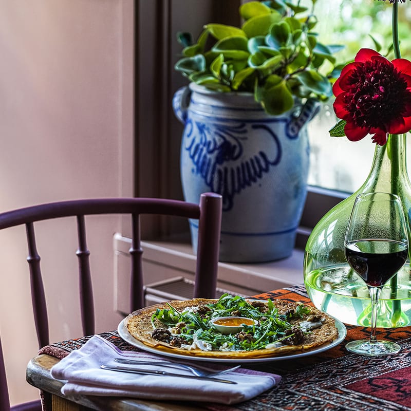 A pancake with rocket and goat cheese on a plate by the window