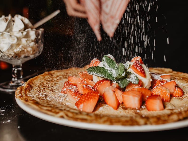 Poedersuiker valt op een pannenkoek met verse aardbeien