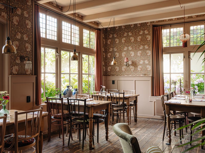 De zaal met behang, hoge ramen en gedekte tafels